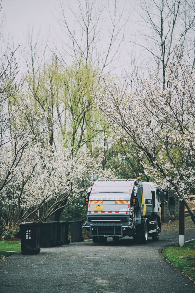 Municipal refuse truck collecting bins on a tree-lined street